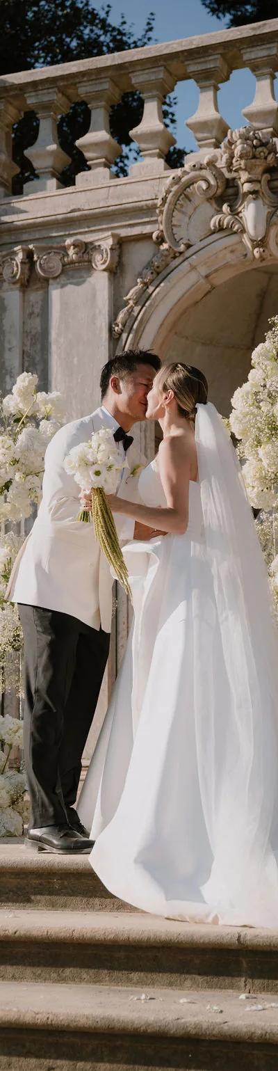 Couple kissing on palace steps under white hydrangea arch